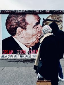 in fotografia il celebre murales del muro di Berlino The Mortal Kiss di Dimitri Vrubel con due persone che passeggiano
