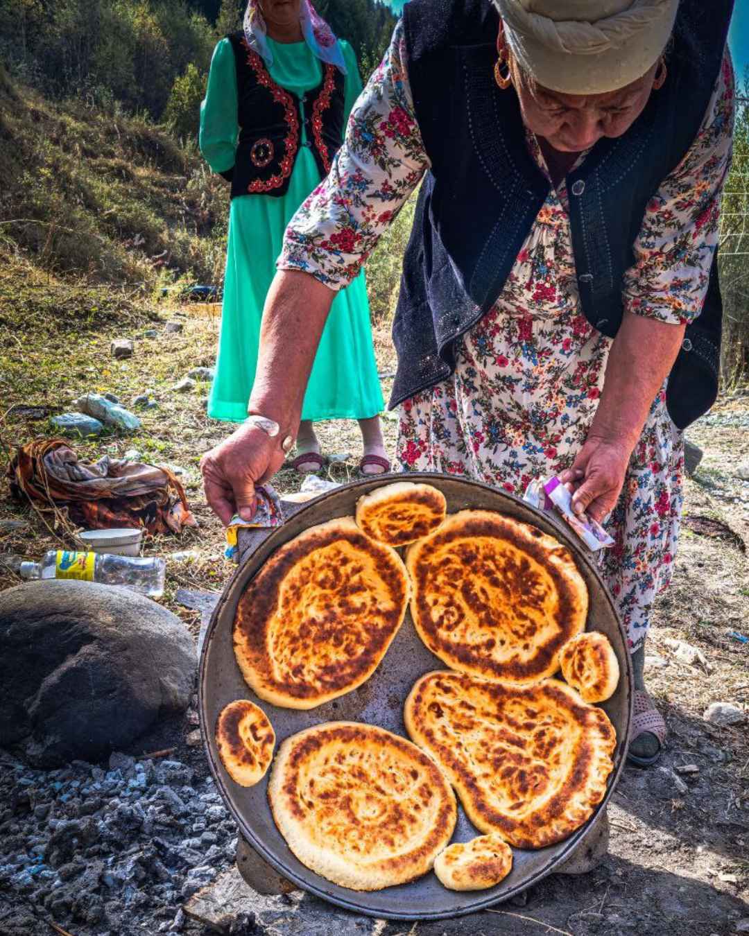 una donna mostra un grande recipiente di ferro con al suo interno pane tipico del kirghizistan